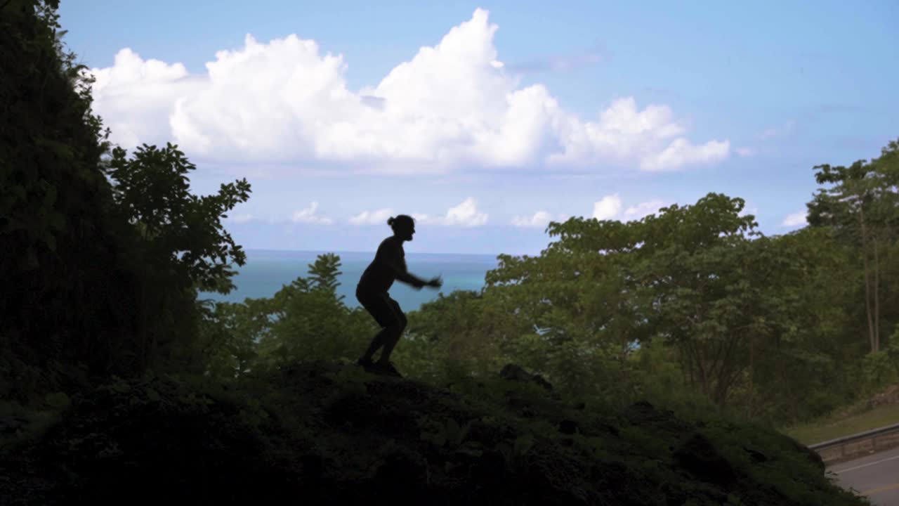 Young men jumping in slow-mo while inside a big cave in siluette with beautiful nature and ocean view in a Caribbean Island road