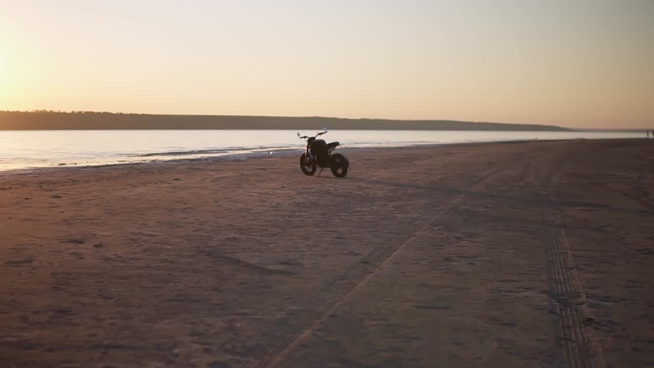 Una moto parcheggiata a terra vicino all'acqua al tramonto con la linea dell'acqua sullo sfondo.