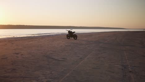 A-motorcycle-parking-on-the-ground-close-to-the-water-in-sunset-with-water-line-on-the-background