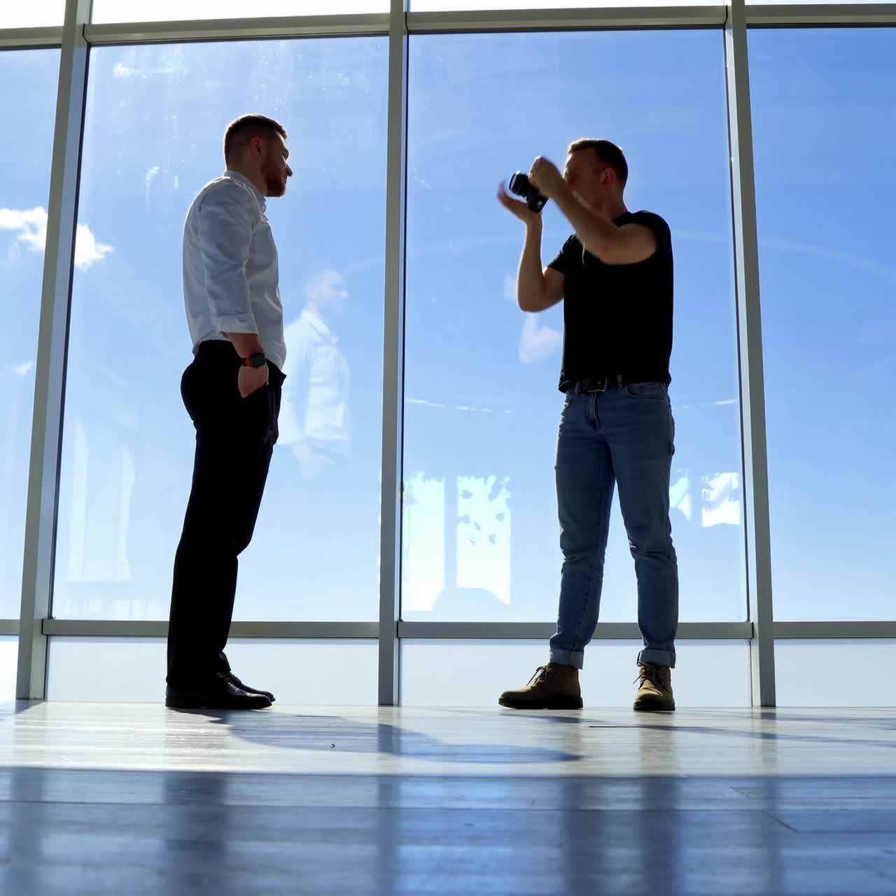 Young businessman posing on camera indoors. Professional photographer and a handsome man on big windows background. View from below