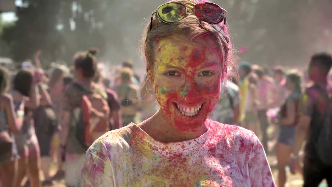 Young happy girl in colourful powder is dancing on holi festival in daytime in summer, watching at camera, color concept, emotional concept