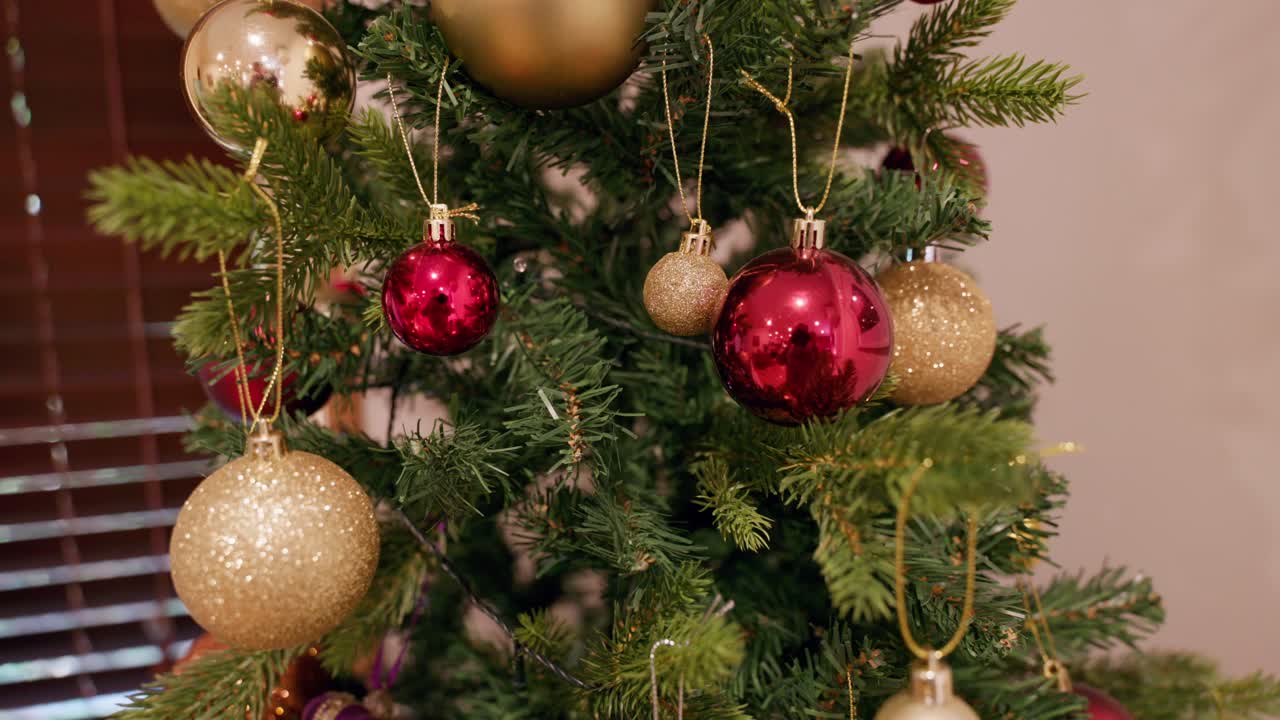 A still, detailed look at red and gold ornaments on a Christmas tree with lights off, focusing on textures.
