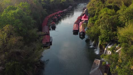 drone shot, flying over a river in thailand in the middle of the jungle, with waterfalls and a charming floating village on the side of the river - sai yok national park - the province of kanchanaburi