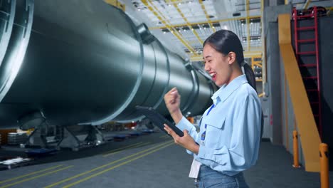 side view of happy asian business woman celebrating using tablet in pipe manufacturing factory