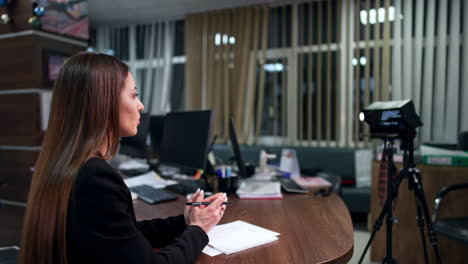 caucasian brunette woman in black jacket talks to camera. blogger reads on-screen display text creating a content. side view.