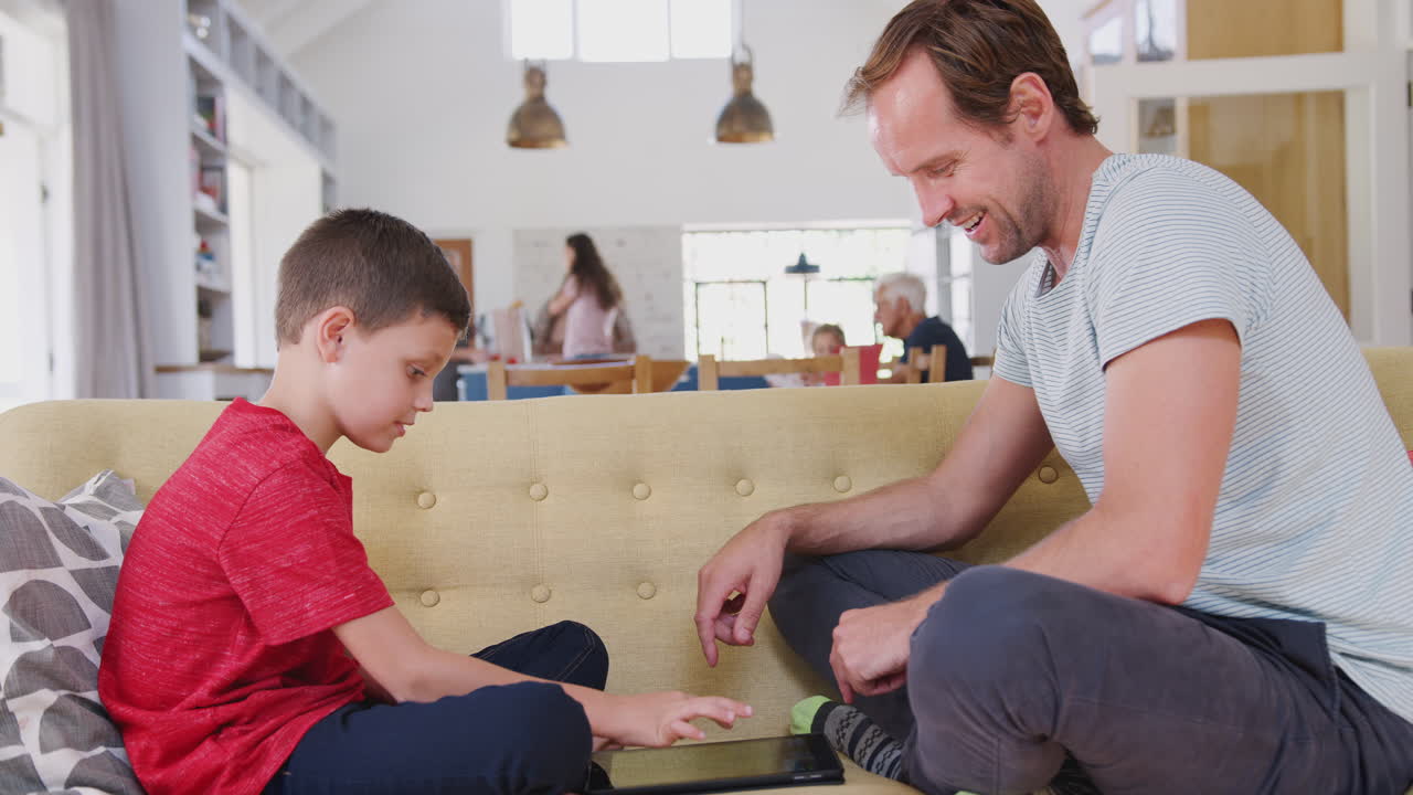 padre sentado con su hijo en el sofá jugando al juego en la tableta digital en casa