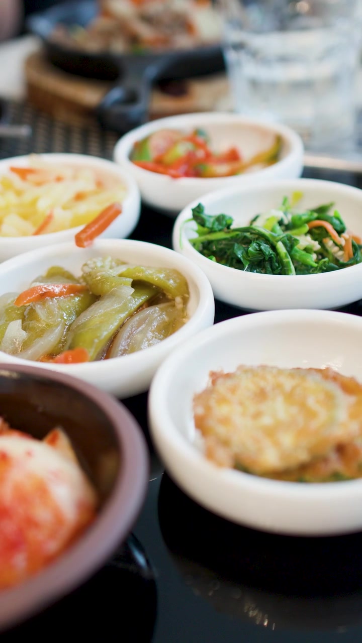 어두운 식탁 위에 김치와 채소를 포함한 다양한 한국 반찬의 클로즈업 샷.