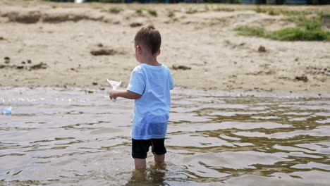 adorable toddler boy standing in the water. little kid plays with watering can and shovel on the beach.