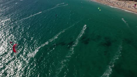 Vista-Aérea-Circular-De-Kitesurfistas-Practicando-Y-Divirtiéndose-Y-Paisaje-En-La-Playa-De-Tarifa,-Cádiz,-España.