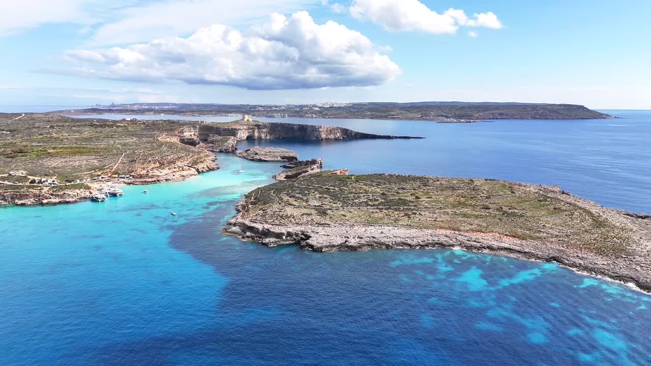 Den blå lagune i Comino, Malta, med grunt turkist vann over kalksteinsbunn mellom øyene Comino og Cominotto, klart Middelhav og ulendt kystlinje, skrått tilbaketrekkende droneopptak