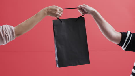 video of hands of caucasian women holding black shopping bag with copy space on red background