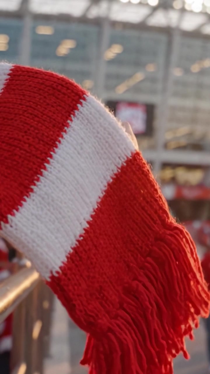 Un tifoso sventola la sua vivace sciarpa rossa e bianca in celebrazione a un evento sportivo, catturando l'atmosfera energica e lo spirito di squadra nello stadio.