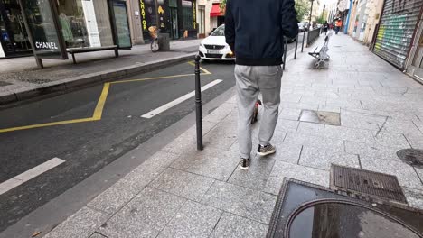 a man and his dog stroll past vehicles and shops.