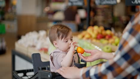 close up a baby girl receives a tangerine from her mother and looks at it in a supermarket while shopping