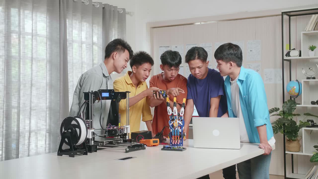 사이보그 손과 3d 프린팅을 가진 젊은 아시아 소년 그룹이 집에서 노트북을 작업하는 동안 회로판에 대해 논의합니다.