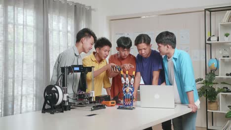 group of young asian boys with a cyborg hand and 3d printing discuss about a circuit board while working on a laptop at home
