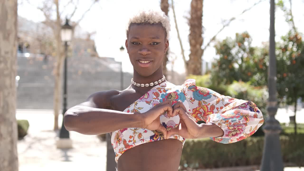 Cheerful black queer person showing heart gesture and smiling on street