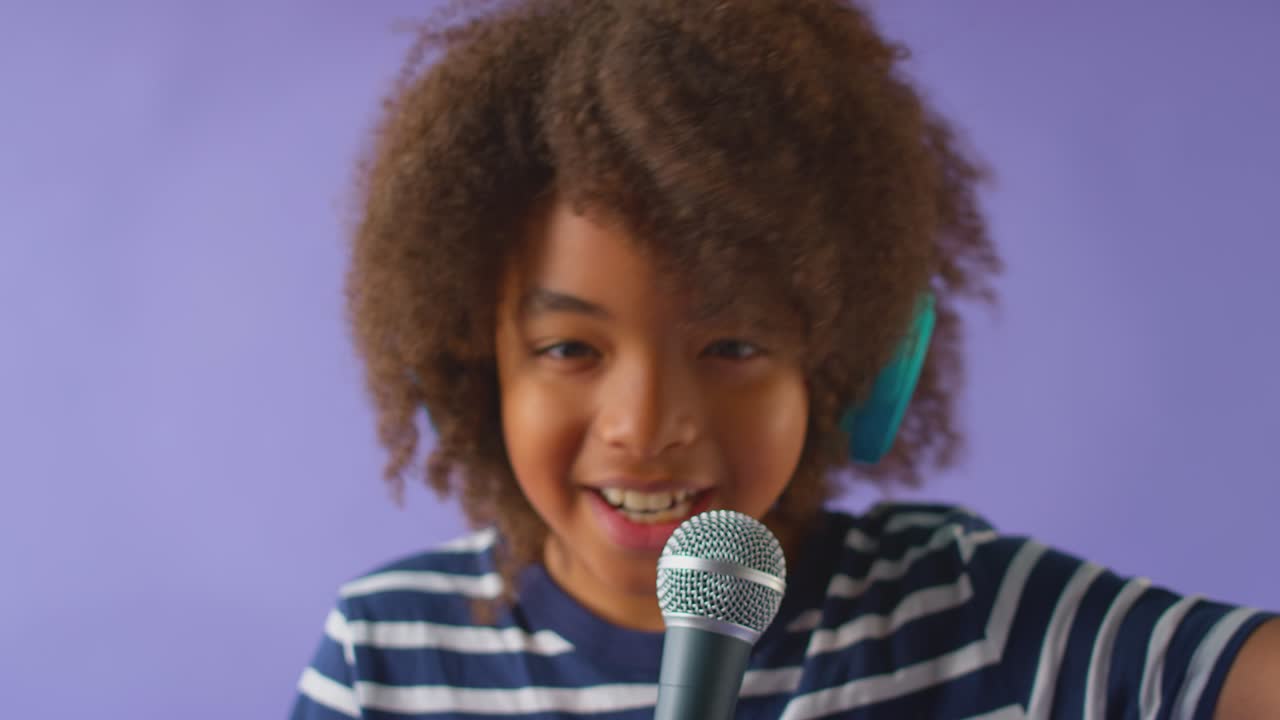 Studio shot of boy with headphones singing karaoke into microphone against purple background - shot in slow motion