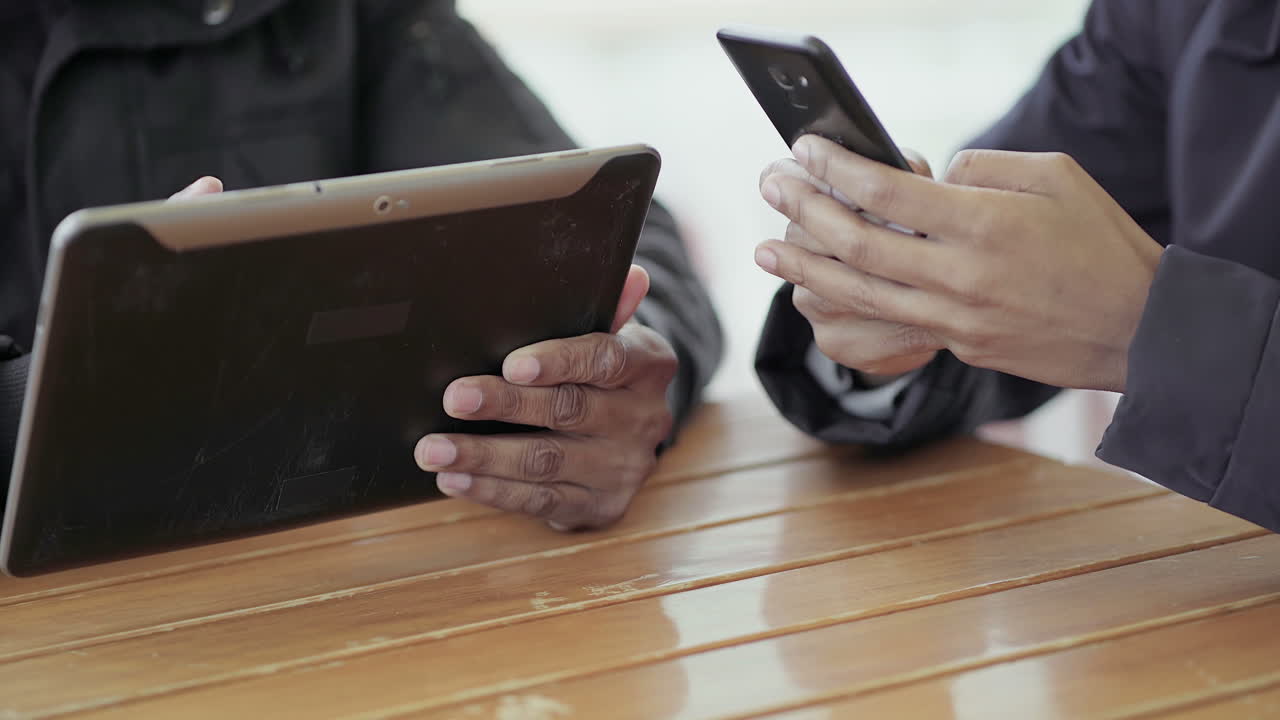 아프리카계 미국인 젊은 소녀들의 손이  ⁇ 드폰에서 구글을 하고 아프리카계 미국인 중년 남자의 손이 태블릿을 사용하고 있습니다.