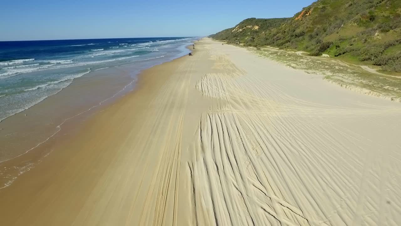 vista a lo largo de las amplias arenas doradas de la isla fraser, con sombras nítidas proyectadas por las pistas 4x4 y un convoy de vehículos con tracción en las cuatro ruedas que circulan por la playa