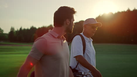 golf players looking sunset on summer field. golfers group walk course fairway.