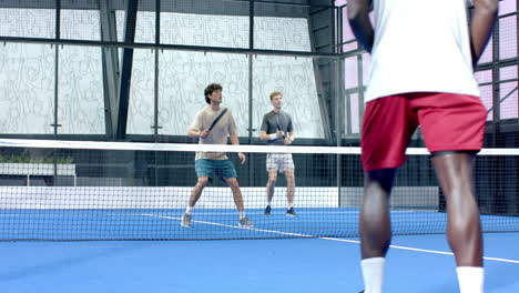 diverse men playing padel tennis on indoor court, focusing on competitive match