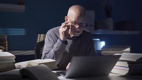 Mature-old-man-reading-book-working-on-laptop,-writing-notes,-analyzing-his-research,-studying.