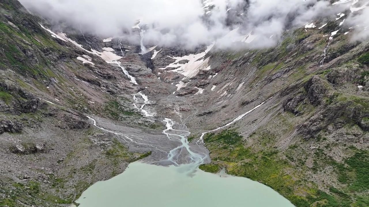Triftgletsjeren smelter ned i søen, med vandløb der strømmer ned ad bjergsiden, omgivet af skyer og klippetoppe i de schweiziske alper, Triftbrücke Triftgletscher, Bern, Schweiz droneudzoomning.