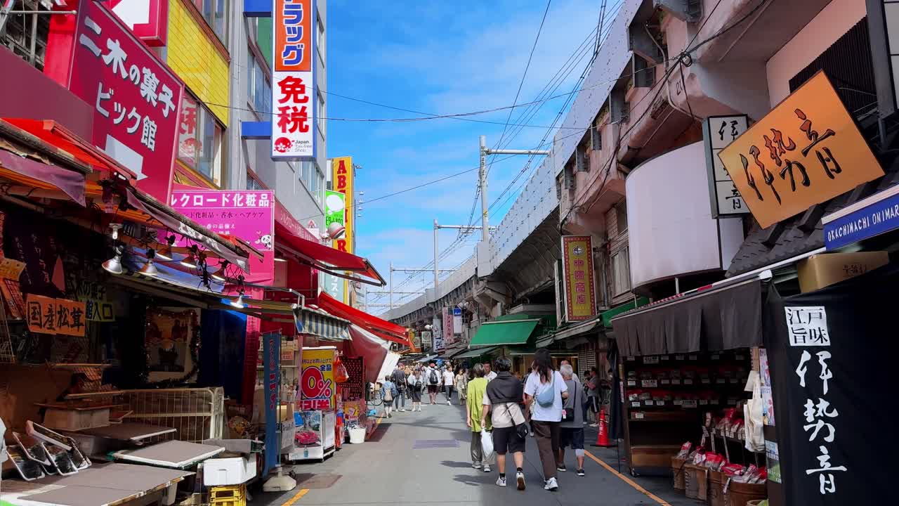 A lively street in a Japanese market with people walking under colorful signs on a sunny day