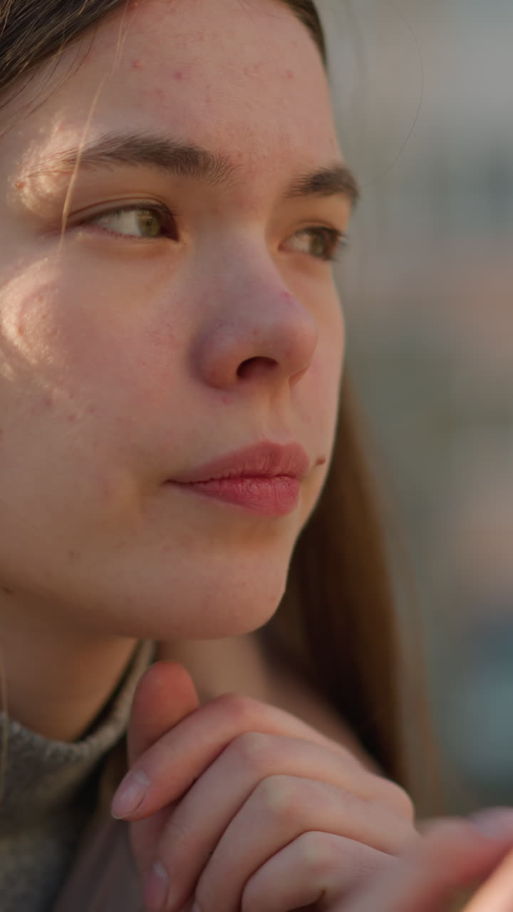 una joven con una chaqueta de melocotón se sienta en un parque, profundamente pensativa con el mentón apoyado en su mano. su expresión es reflexiva, mientras medita en silencio en el tranquilo entorno al aire libre