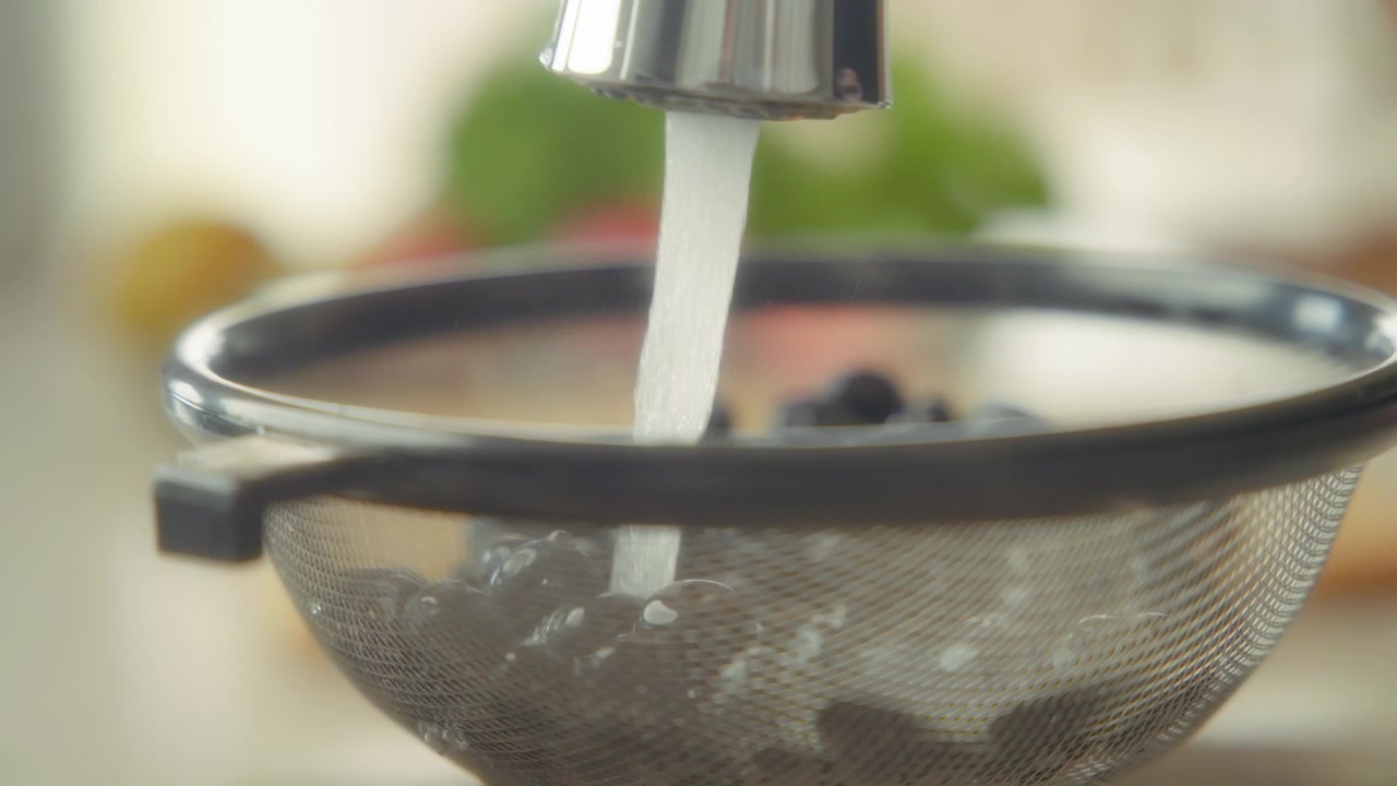 Primo piano di mirtilli lavati sotto acqua corrente in uno scolapasta.