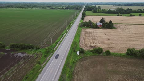 Car-Driving-On-Countryside-Road-Among-Agricultural-Fields---aerial-shot
