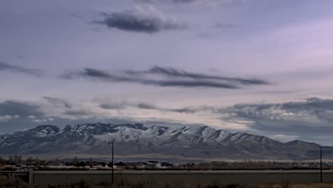 Stormy-clouds-over-the-snowy-mountains-beyond-the-busy-highway---zoom-out-time-lapse