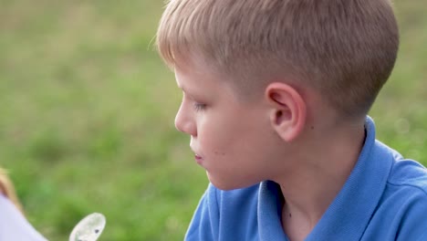 a blond-haired boy in a blue t-shirt eats ice cream with a plastic spoon in nature. close-up. slow motion