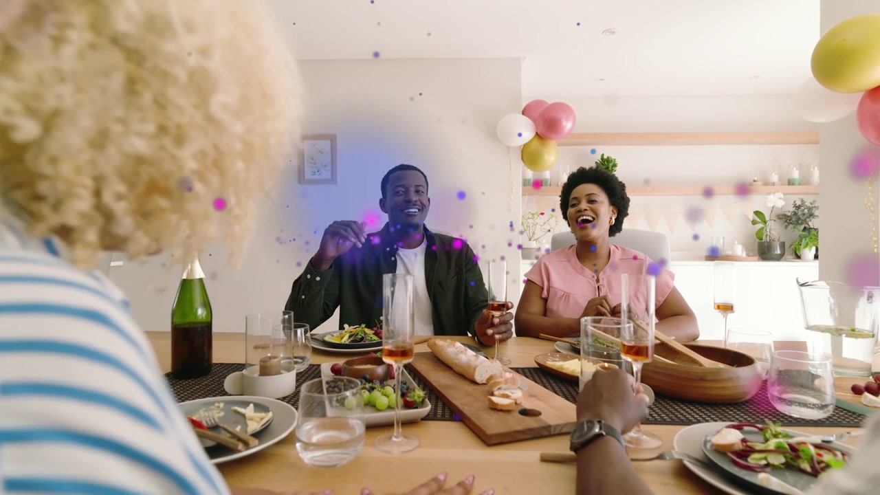 Homme portant un toast, groupe célébrant, riant et trinquant autour d'un buffet, avec une superposition de confettis s'élevant.