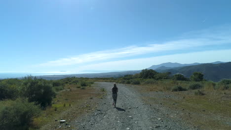 Aerial-tracking-shot-of-woman-jogging-in-the-mountains-on-a-sunny-day