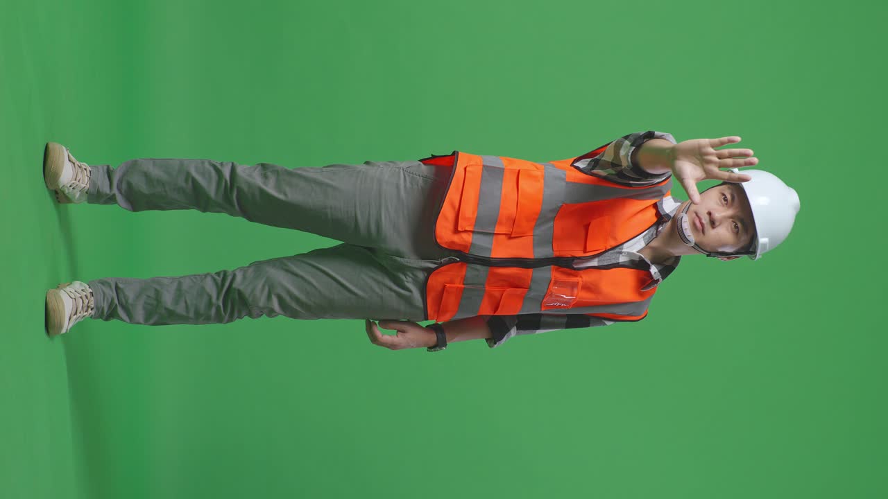 안전 헬을 입은 아시아 남성 엔지니어의 몸 전체가 녹색 스크린 배경 스튜디오에 서있는 동안 손 표시 없이 불쾌감을 표합니다.