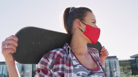 mujer caucásica con máscara facial sosteniendo patinetas en un día soleado