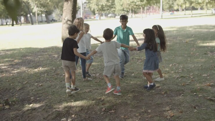 Crianças felizes de mãos dadas, dançando em roda e brincando de roda-roda no parque.