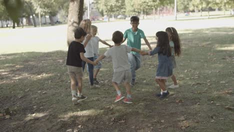 happy kids holding hands, round dancing and playing playing ring a ring o' roses in the park