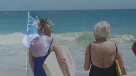 standing on beach, two older women holding surfboards with australian flag animation