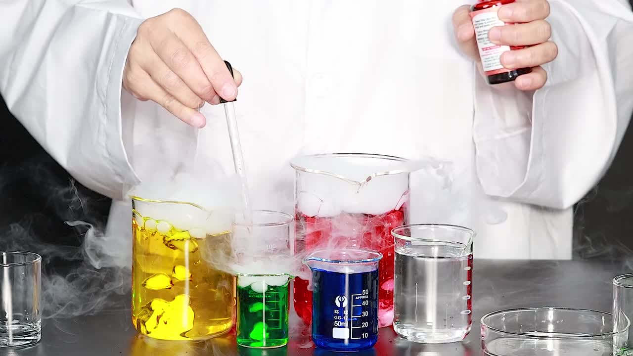 Close-up of a scientist adding liquid to beakers creating colorful reactions and thick white smoke