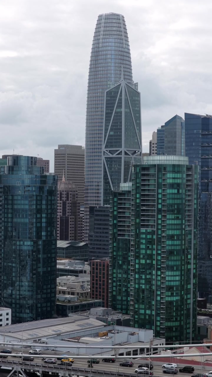 La Salesforce Tower si erge accanto alla facciata a diagrid del grattacielo 181 Fremont, torri di vetro che perforano il cielo coperto sopra lo skyline del distretto finanziario di San Francisco vicino al centro. Ripresa aerea verticale con drone.