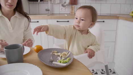 linda niña sentada en una silla alta en la cocina mientras su madre la alimenta 1