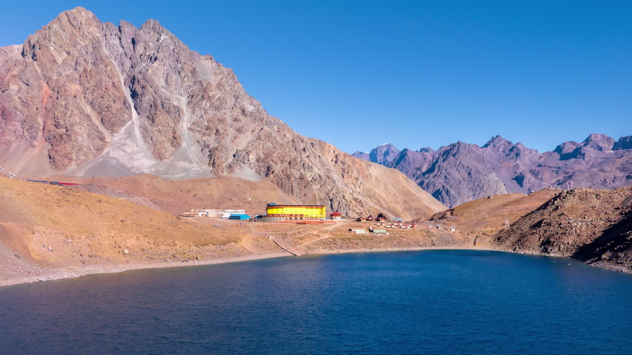 Zoom in hyperlapse approaching Andean lake with blue water and colorful buildings surrounded by mountains in Chile