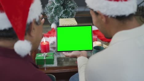 Biracial-father-with-son-in-santa-hats-making-tablet-christmas-video-call,-with-green-screen