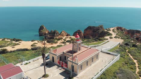 red lighthouse at the end of the ponta da piedade in lagos, algarve, portugal - aerial orbit point of interest