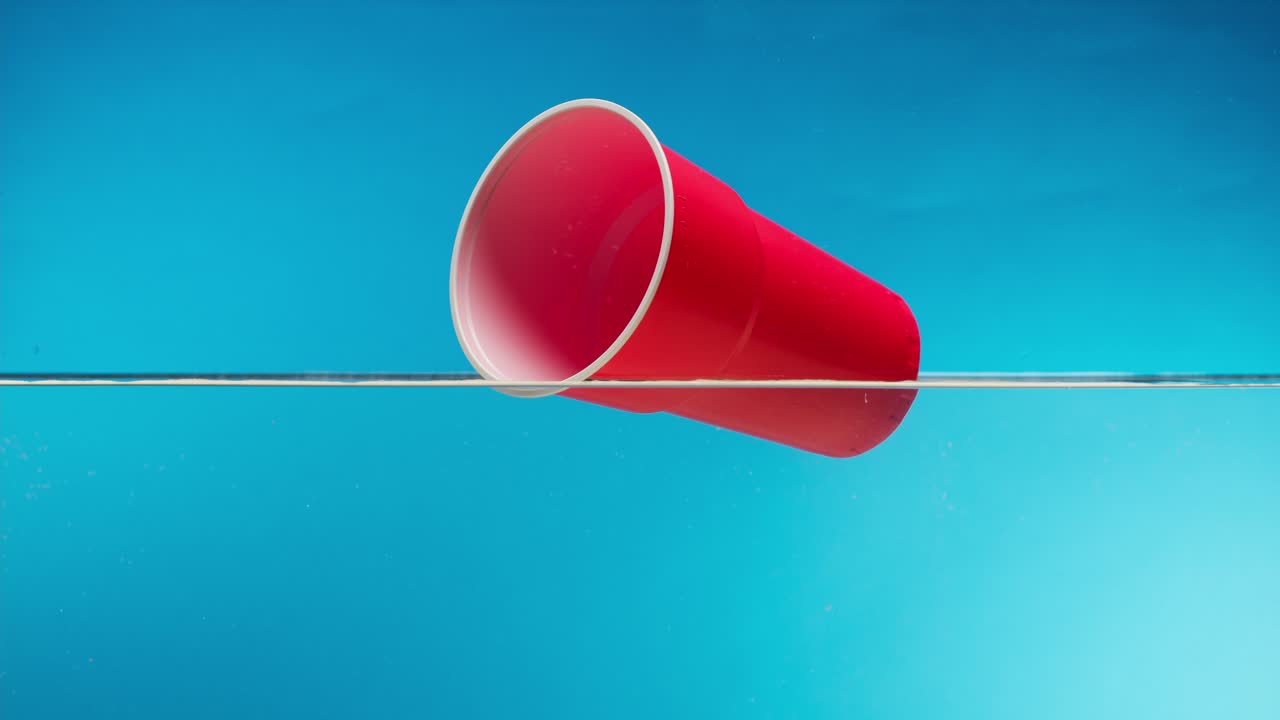 Bicchiere di plastica rosso che galleggia sull'acqua con sfondo blu
