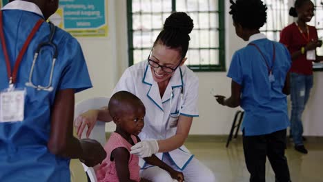caring female doctor interacts with a young child, conducting a gentle examination in a bustling community health center, while other children wait patiently in the background