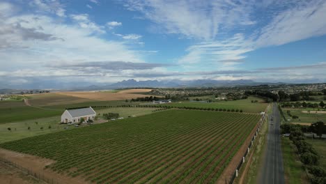 roadside-vineyard-with-white-farmhouse-in-Franschoek-South-Africa,-aerial